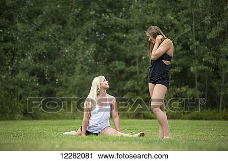 Stock Image - Two teenage gymnasts pausing to talk while doing stretches for their gymnastics routine; Edmonton, Alberta, Canada. Fotosearch