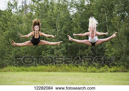 Two teenage gymnasts practicing their routines outdoors in a park, doing split jumps; Edmonton, Alberta, Canada View Large Photo Image Picture - Two teenage gymnasts practicing their routines outdoors in a park, doing split jumps; Edmonton, Alberta, Canada. Fotosearch