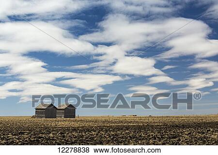 Stock Photo - Two wooden sheds in a stubble field with dramatic clouds and blue sky; Alberta, Canada. Fotosearch