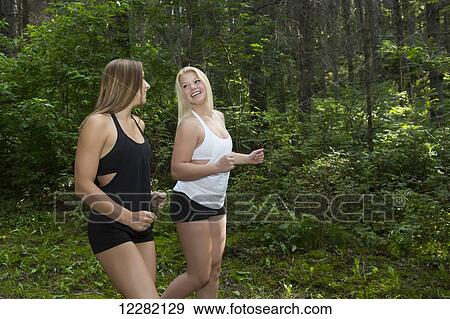 Stock Photo - Two young athletic girls jogging in the woods in a park; Edmonton, Alberta, Canada. Fotosearch