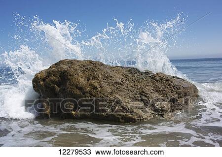 Stock Image - Waves crashing and splashing on a large rock at the water's edge; South Shields, Tyne and Wear, England. Fotosearch