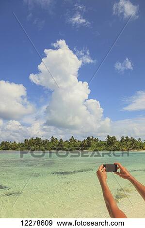 Stock Photo - Woman taking a picture of an atoll with a smart phone; Medahutthaa Island, North Huvadhoo Atoll, Southern Maldives. Fotosearch