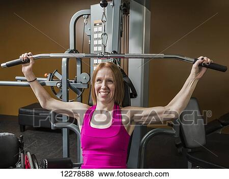 Young disabled woman using a shoulder press to rehabilitate herself from a spinal injury; Edmonton, Alberta, Canada View Large Photo Image Stock Photo - Young disabled woman using a shoulder press to rehabilitate herself from a spinal injury; Edmonton, Alberta, Canada. Fotosearch