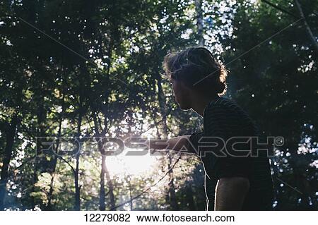 Stock Image - Young man reaching out to the sunlight in a forest, Little River State Park; Waterbury, Vermont, United States of America. Fotosearch