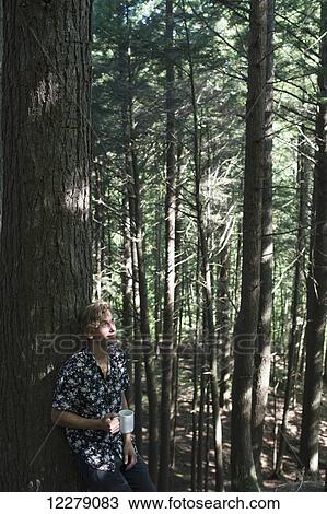 Stock Image - Young man standing in a forest with a cup of coffee, Little River State Park; Waterbury, Vermont, United States of America. Fotosearch