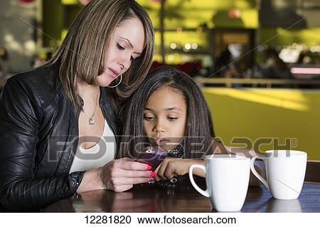 Young mother and her daughter in a cafe looking at a smart phone while taking a break from shopping; St. Albert, Alberta, Canada View Large Photo Image Stock Image - Young mother and her daughter in a cafe looking at a smart phone while taking a break from shopping; St. Albert, Alberta, Canada. Fotosearch