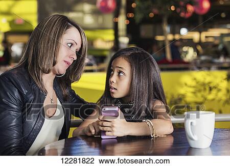 Young mother and her daughter in a cafe looking at a smart phone while taking a break from shopping and being concerned about content being viewed; St. Albert, Alberta, Canada View Large Photo Image Stock Image - Young mother and her daughter in a cafe looking at a smart phone while taking a break from shopping and being concerned about content being viewed; St. Albert, Alberta, Canada. Fotosearch