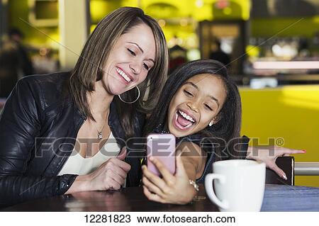 Young mother and her daughter in a cafe looking at a smart phone and taking a selfie while taking a break from shopping; St. Albert, Alberta, Canada View Large Photo Image Stock Image - Young mother and her daughter in a cafe looking at a smart phone and taking a selfie while taking a break from shopping; St. Albert, Alberta, Canada. Fotosearch