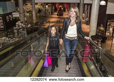 Picture - Young mother and her daughter using an escalator in a shopping complex; St. Albert, Alberta, Canada. Fotosearch