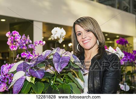 Stock Photo - Young woman admiring flowers in a greenhouse section of a shopping complex; St. Albert, Alberta, Canada. Fotosearch