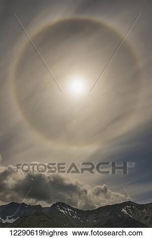 Stock Photograph - A 22 degree halo fills the sky over the Chigmit Mountains within Lake Clark National Park & Preserve, Alaska.. Fotosearch