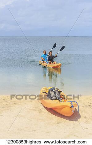 Stock Photograph - A couple arriving at the beach in a kayak, Saint Georges Caye Resort; Belize City, Belize. Fotosearch