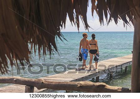 A couple walks on a wooden dock with snorkelling gear, Saint Georges Caye Resort; Belize City, Belize View Large Photo Image Stock Photograph - A couple walks on a wooden dock with snorkelling gear, Saint Georges Caye Resort; Belize City, Belize. Fotosearch