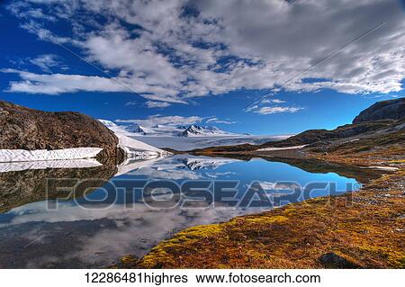 Stock Photograph - A crystal clear lake near the Harding Icefield Trail with the Harding Ice Field in the background, Kenai Fjords National Park; Alaska, United States of America. Fotosearch