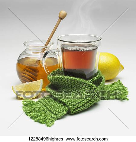 Stock Photograph - A cup of steaming hot tea tied with a scarf with a pot of honey and lemon; Toronto, Ontario, Canada. Fotosearch