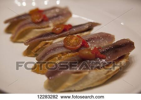 A dish of pintxos in a bar with anchovies, tomatoes and fish roe on bread; San Sebastian, Spain View Large Photo Image Stock Image - A dish of pintxos in a bar with anchovies, tomatoes and fish roe on bread; San Sebastian, Spain. Fotosearch