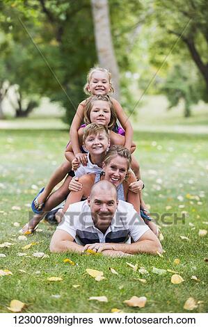 Stock Photograph - A family creating a totem pole picture by climbing on top of each other in a park; Edmonton, Alberta, Canada. Fotosearch