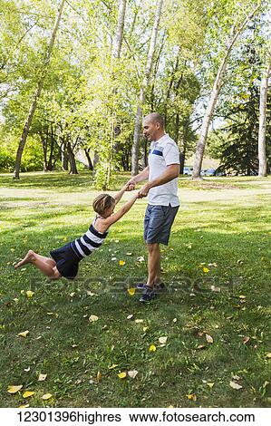Stock Photograph - A father swinging his daughter around in a park during a family outing; Edmonton, Alberta, Canada. Fotosearch
