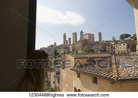 A female tourist looks out the window at the walled medieval village of San Gimignano; San Gimignano, Province of Siena, Tuscany, Italy View Large Photo Image Stock Photograph - A female tourist looks out the window at the walled medieval village of San Gimignano; San Gimignano, Province of Siena, Tuscany, Italy. Fotosearch