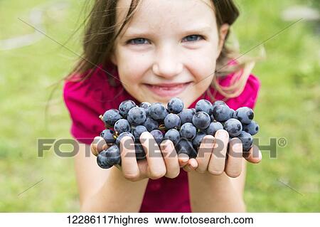 Stock Photograph - A girl with handfuls of grapes; Salmon Arm, British Columbia, Canada. Fotosearch