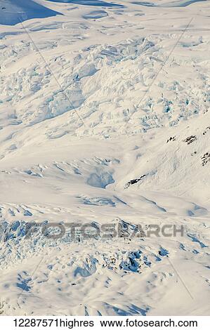 Stock Photograph - A glacier hangs in a valley below jagged snow covered peaks in Kings Bay, Prince William Sound; Whittier, Alaska, United States of America. Fotosearch