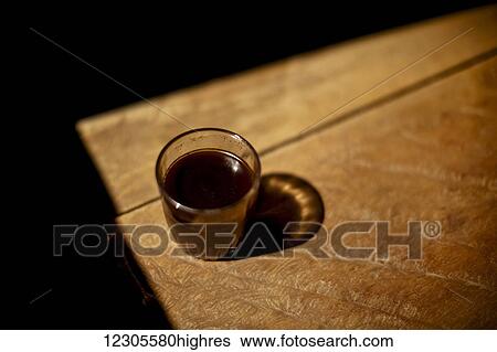 Stock Photograph - A glass of hot coffee sits in the sunlight, made from beans roasted and ground with a wooden mortar not 200 feet away. Muara Pinang is a huge coffee producing village; Sumatra, Indonesia. Fotosearch