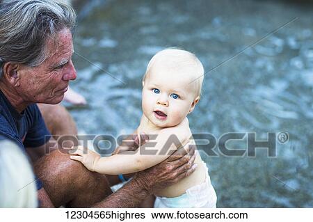 Stock Photograph - A grandfather holds a young baby at the poolside; Fountain Valley, California, United States of America. Fotosearch