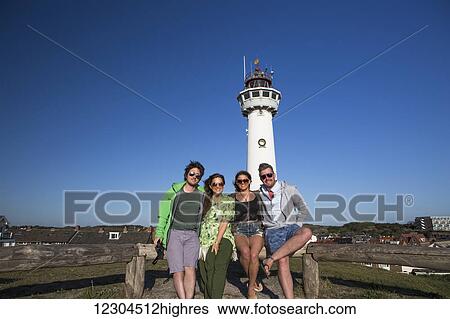 A group of friends standing with a lighthouse in the background outside of Amsterdam central; Egmond aan Zee, Holland View Large Photo Image Stock Photograph - A group of friends standing with a lighthouse in the background outside of Amsterdam central; Egmond aan Zee, Holland. Fotosearch