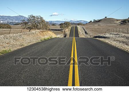 Stock Photograph - A hilly road with double solid yellow lines leading into the distance in a rural area, near Santa Ynez; California, United States of America. Fotosearch