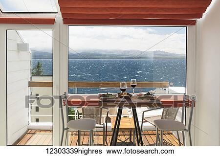 A lunch table with two glasses of red wine is set in front of the balcony window of a bright apartment with view over a lake; Bariloche, Argentina View Large Photo Image Stock Photograph - A lunch table with two glasses of red wine is set in front of the balcony window of a bright apartment with view over a lake; Bariloche, Argentina. Fotosearch