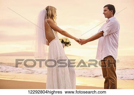 Stock Photograph - A married couple, bride and groom, at sunset on a beautiful tropical beach. Fotosearch