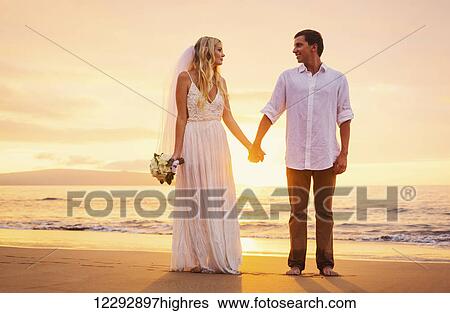 Stock Photograph - A married couple, bride and groom, at sunset on a beautiful tropical beach. Fotosearch
