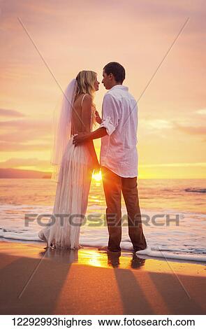 Stock Photograph - A married couple, bride and groom, at sunset on a beautiful tropical beach. Fotosearch