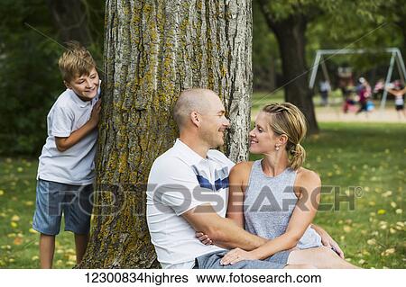 A married couple spending quality time together in a park during a family outing with their son peeking from behind a tree; Edmonton, Alberta, Canada View Large Photo Image Stock Photograph - A married couple spending quality time together in a park during a family outing with their son peeking from behind a tree; Edmonton, Alberta, Canada. Fotosearch