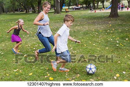 Stock Photograph - A mother playing soccer with her kids in a park during a family outing; Edmonton, Alberta, Canada. Fotosearch