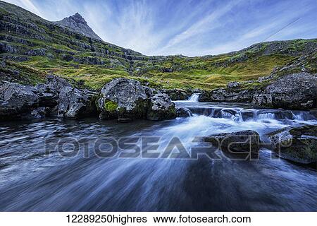 Stock Photograph - A mountain stream runs toward the ocean in the fjord called Mjoifjordur, East Iceland; Iceland. Fotosearch