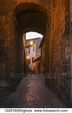 A narrow covered walkway of cobblestone leading to a light and houses at dusk; Orvieto, Umbria, Italy View Large Photo Image Stock Photograph - A narrow covered walkway of cobblestone leading to a light and houses at dusk; Orvieto, Umbria, Italy. Fotosearch