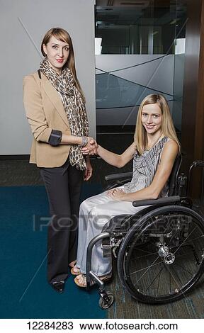 Stock Image - A professional business woman shaking hands and posing with a young paraplegic woman in a wheelchair; St. Albert, Alberta, Canada. Fotosearch
