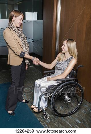Stock Photo - A professional business woman shaking hands with a young paraplegic woman in a wheelchair; St. Albert, Alberta, Canada. Fotosearch