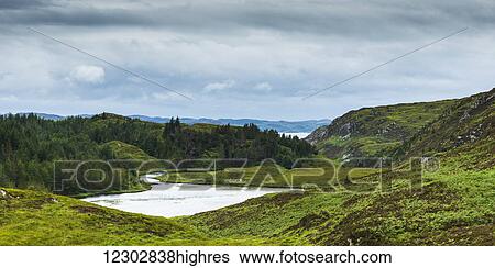 Stock Photograph - A river flowing into a pond surrounded by lush grass and forest in the Highlands; Scotland. Fotosearch