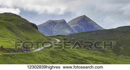 A road winding through the mountains with two mountain peaks under a cloudy sky in the Highlands; Scotland View Large Photo Image Stock Photograph - A road winding through the mountains with two mountain peaks under a cloudy sky in the Highlands; Scotland. Fotosearch