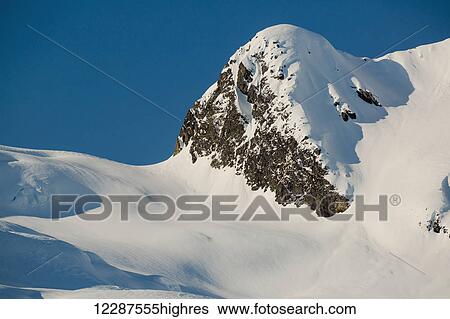 Stock Photograph - A rocky peak is blanketed in a fresh layer of snow, late afternoon light casting deep shadows on the landscape, Kings Bay, Prince William Sound; Whittier, Alaska, United States of America. Fotosearch