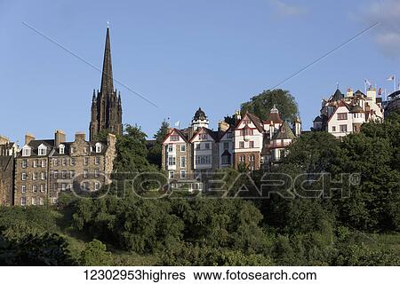 Stock Photograph - A tower of a church with a cross against a blue sky and residential buildings in front of it; Edinburgh, Scotland. Fotosearch