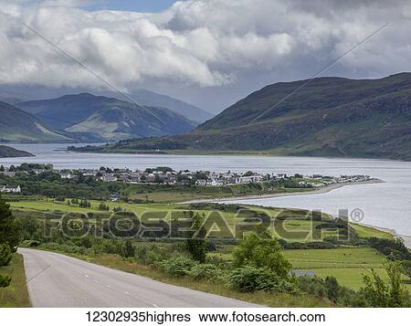 Stock Photograph - A town along the water with mountains under a cloudy sky; Scotland. Fotosearch