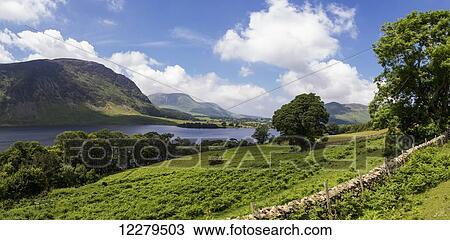 Stock Image - A tranquil lake by mountains and a stone wall in the foreground; Cumbria, England. Fotosearch