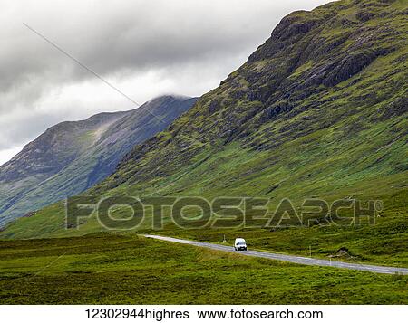 A vehicle travels on a road beside rugged mountains under a cloudy sky; Scotland View Large Photo Image Stock Photograph - A vehicle travels on a road beside rugged mountains under a cloudy sky; Scotland. Fotosearch