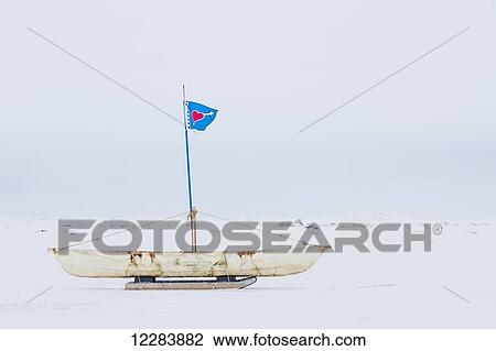 Stock Image - A white Umiak skin boat sits on skids on the sea ice with a flag flying above the boat, Barrow, North Slope, Arctic Alaska, USA, Winter. Fotosearch