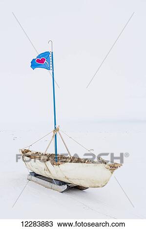 Stock Image - A white Umiak skin boat sits on skids on the sea ice with a flag flying above the boat, Barrow, North Slope, Arctic Alaska, USA, Winter. Fotosearch