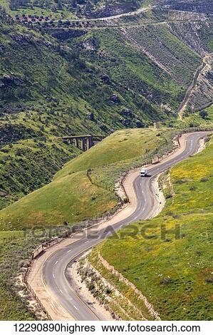 Stock Photograph - A winding road that makes it's way up and and around the Golan Heights, with remains of a train track bridge built over the Yarmouk river in the distance; Golan Heights, Israel. Fotosearch