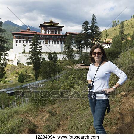 Picture - A woman poses with Rinpung Dzong in the background; Paro, Bhutan. Fotosearch